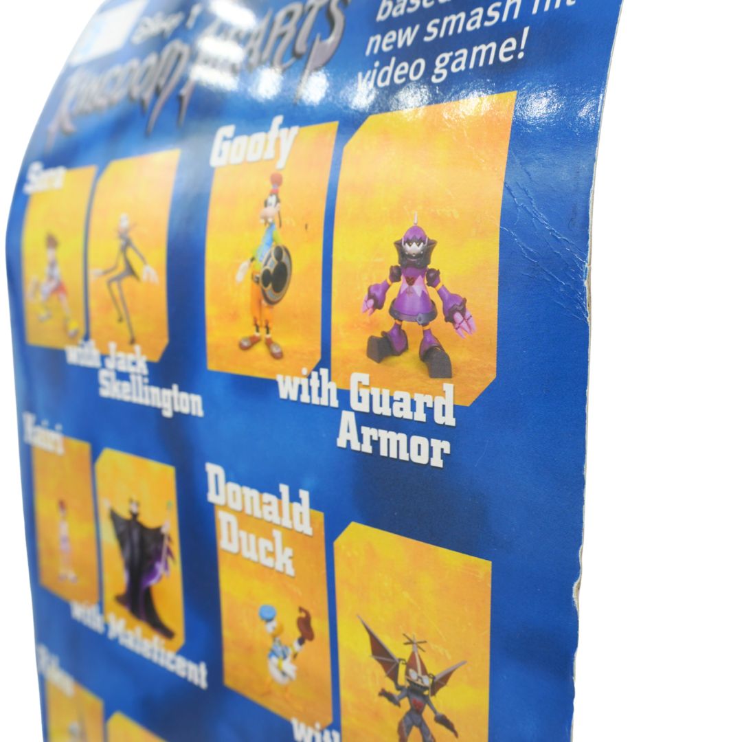 Close-up of a blue collectible character card or poster showing Disney Kingdoms characters including Goofy with Shield, a purple guard character, Donald Duck, and others on a white background.