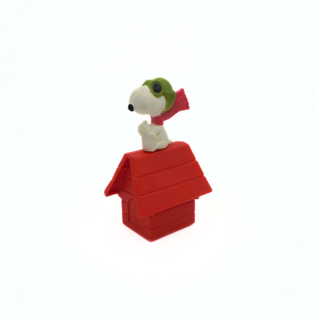 Snoopy figurine on a red doghouse with a green hat and red scarf on a white background