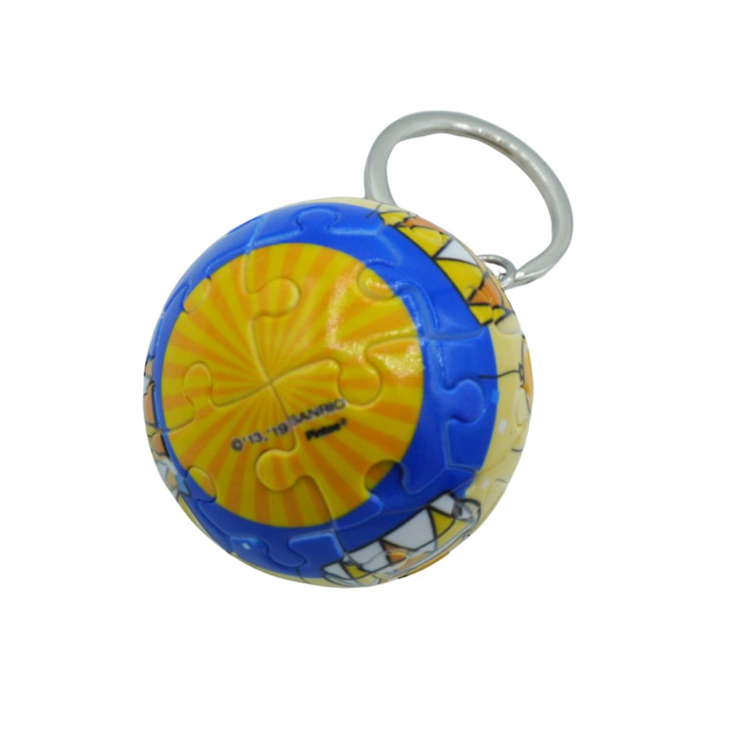 A small spherical keychain featuring a yellow and blue puzzle-piece design with a cartoon character graphic, attached to a silver metal key ring, shown on a plain white background.