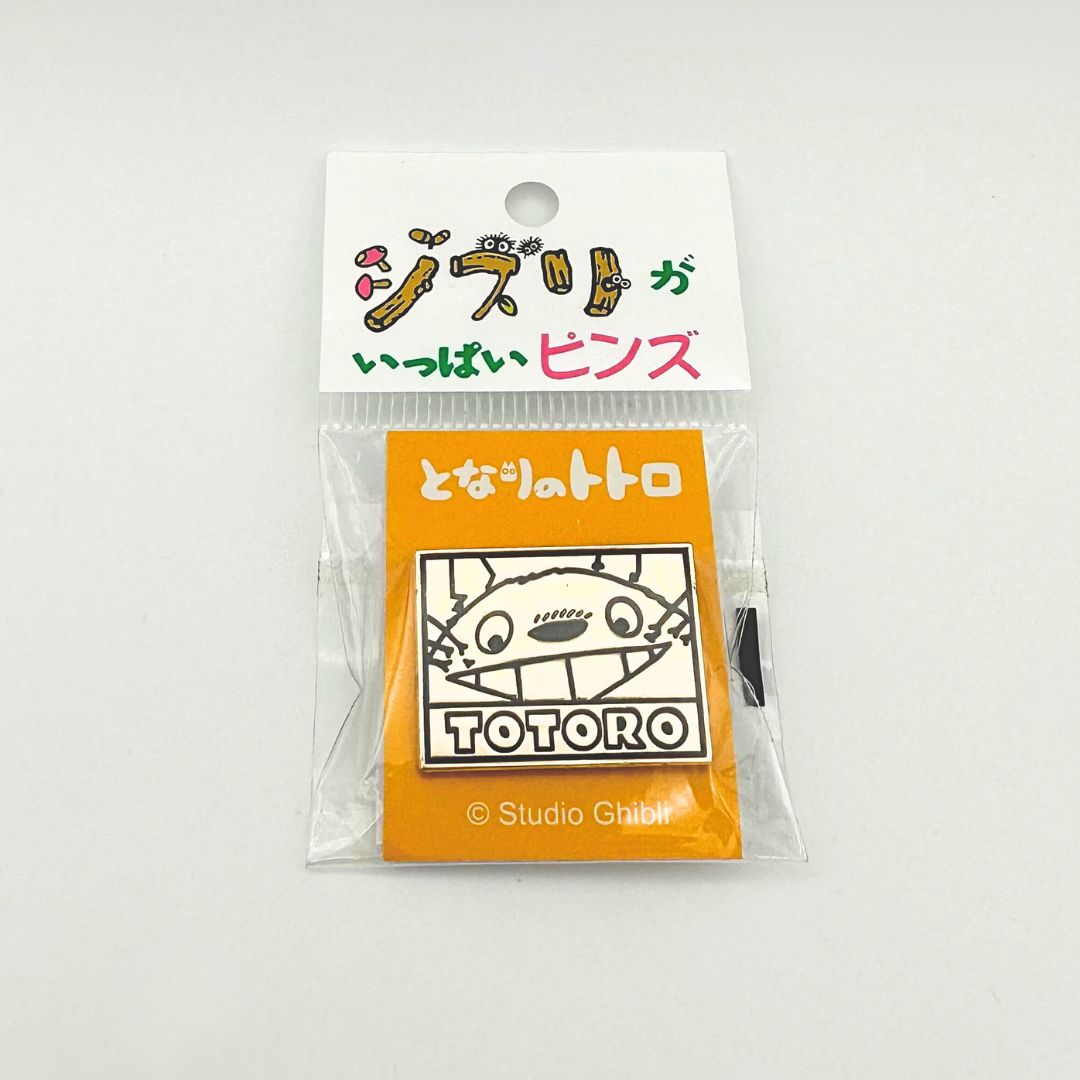 A gold toned Totoro pin on its original cardback and inside plastic packaging, featuring branding of Studio Ghibli