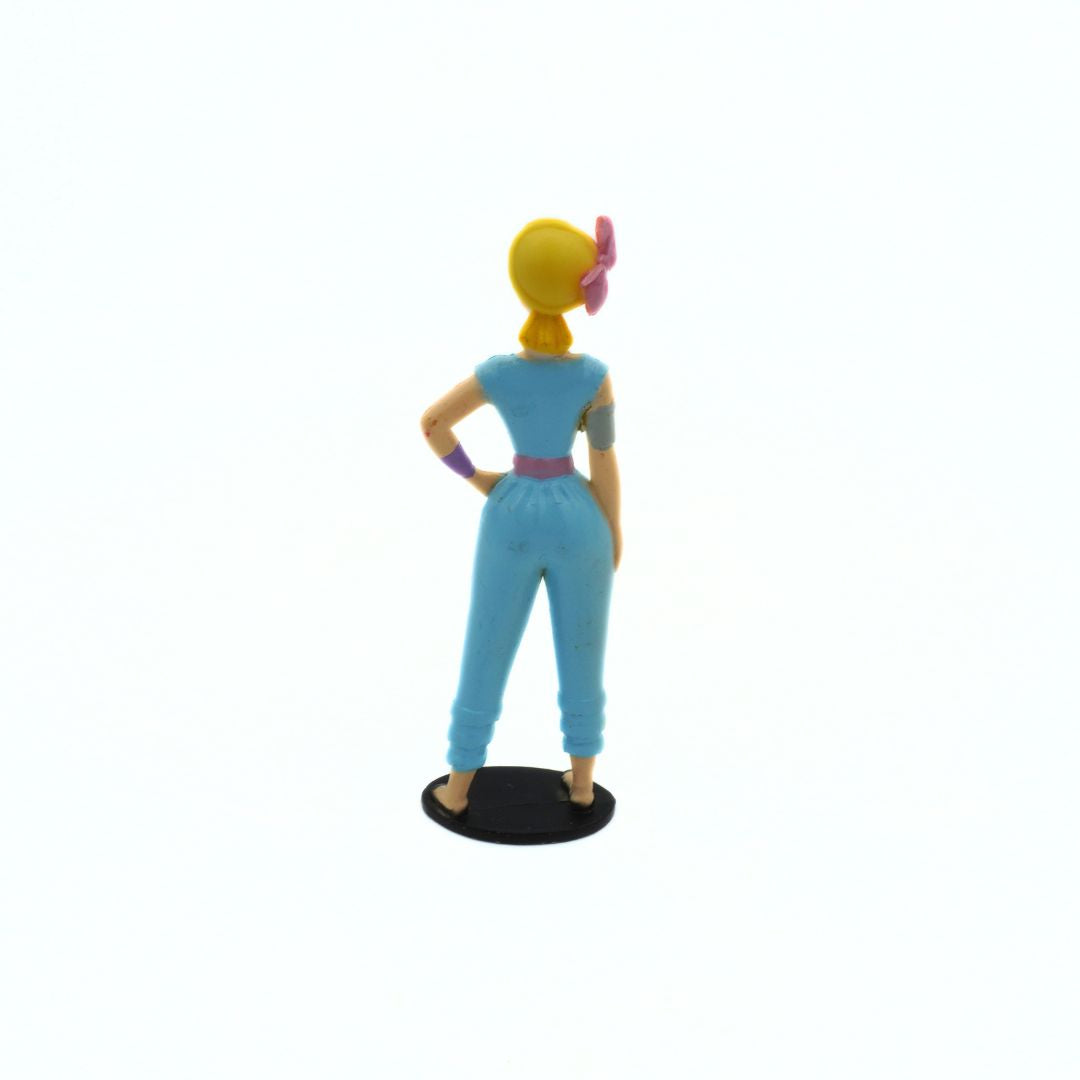 Toy figure of a character in a blue outfit with a pink accessory on a white background