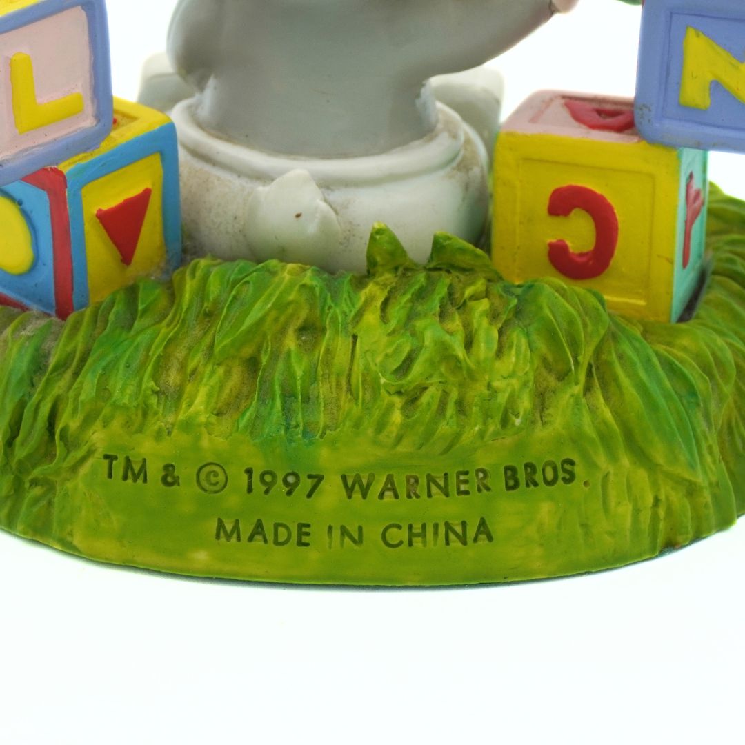 Toy figure with colorful blocks and grass-like base, Warner Bros. branding visible.
