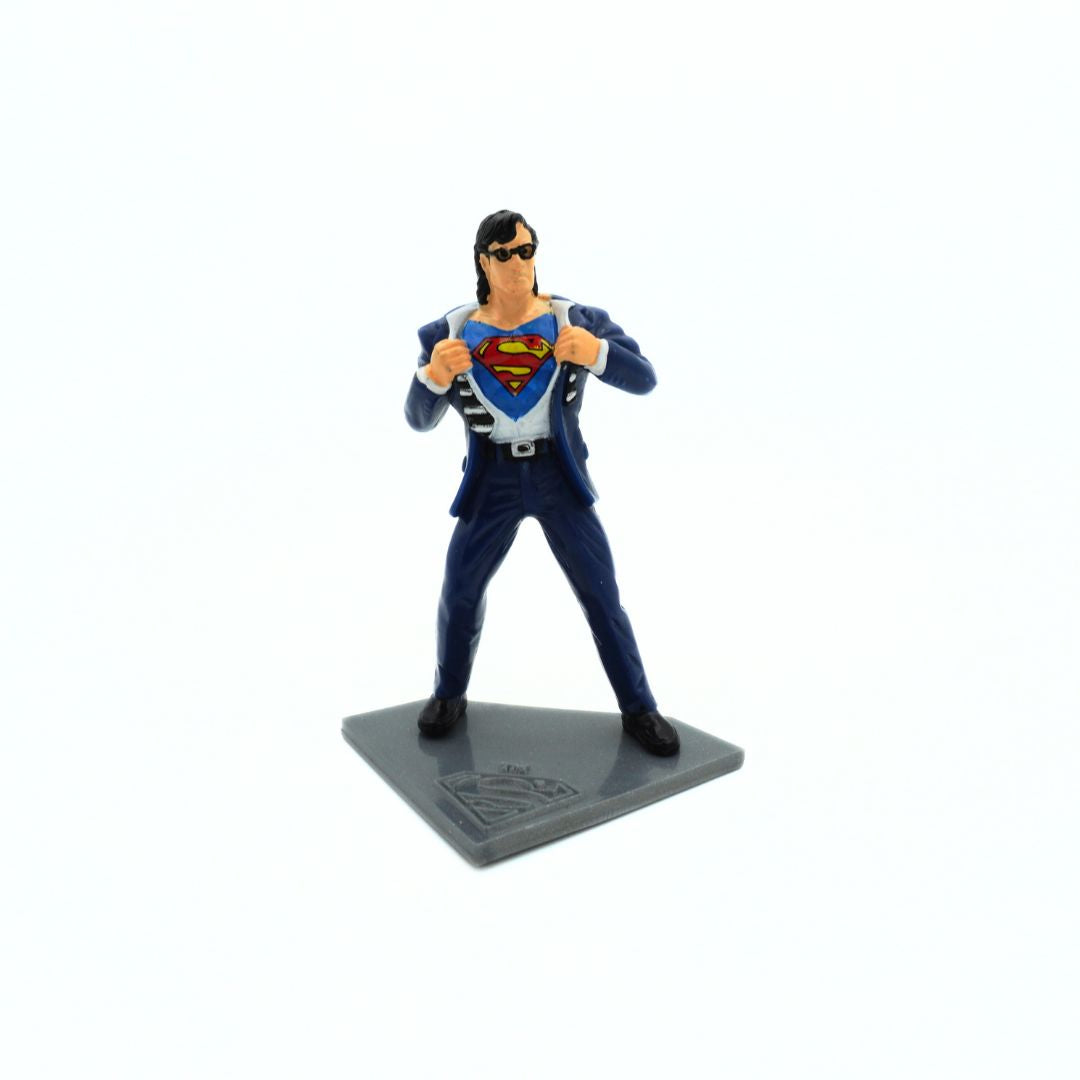 A vintage 90s Clark Kent transforming into Superman figurine on a grey stand