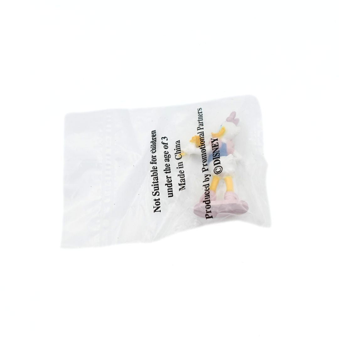 Photo of the back of a Daisy Duck cake topper still in its original packaging, on a pinkish purple platform and holding a yellow flower