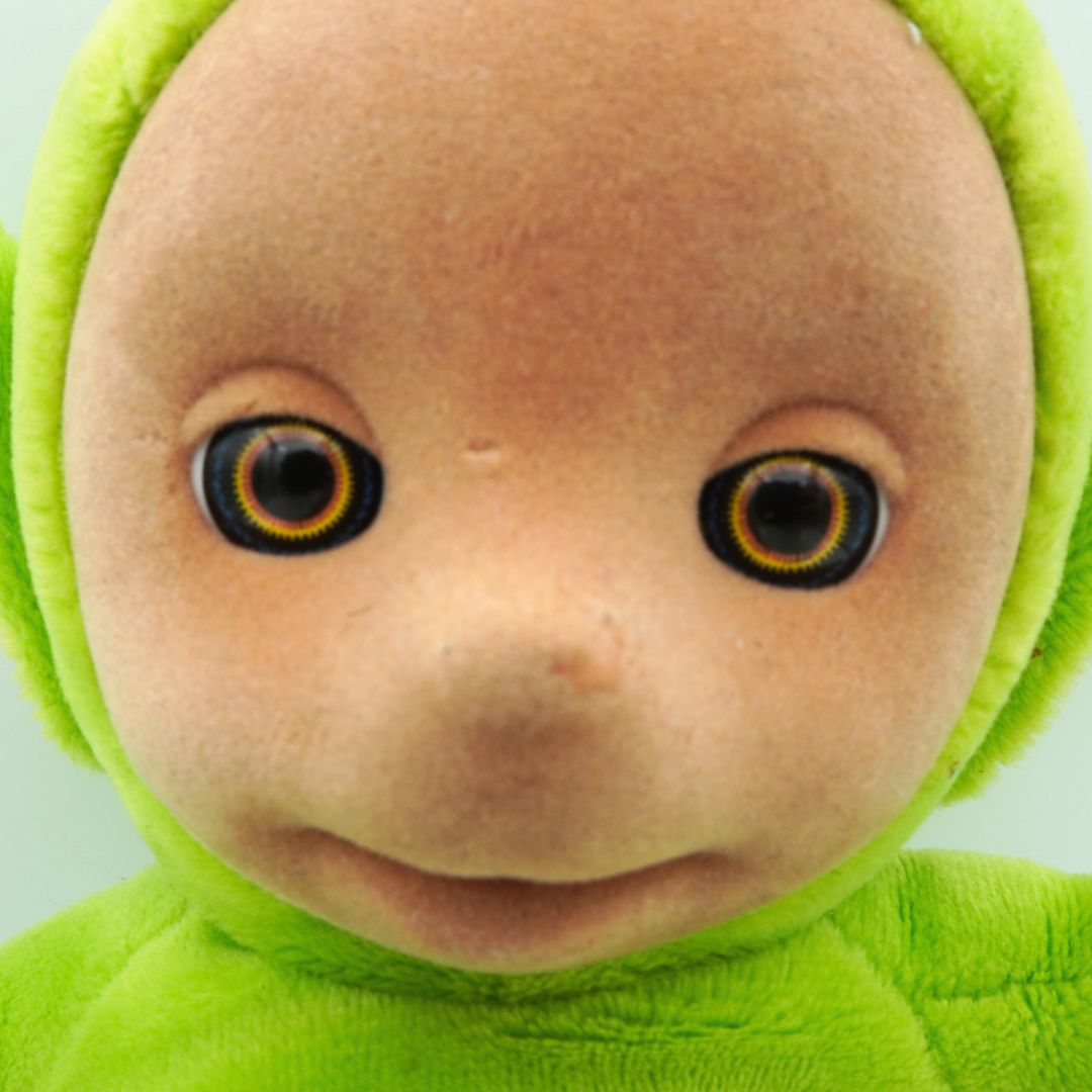 Close-up of a plush Dipsy toy with a green outfit and brown face.