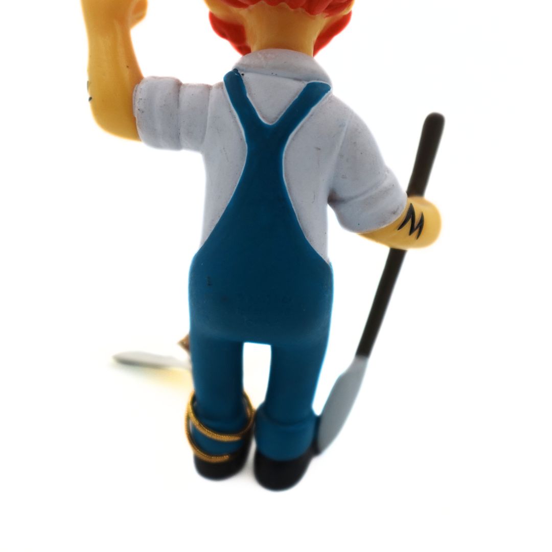 Close up of the back of a 2005 Simpsons figurine showing Groundskeeper Willie with a shovel and blue overalls