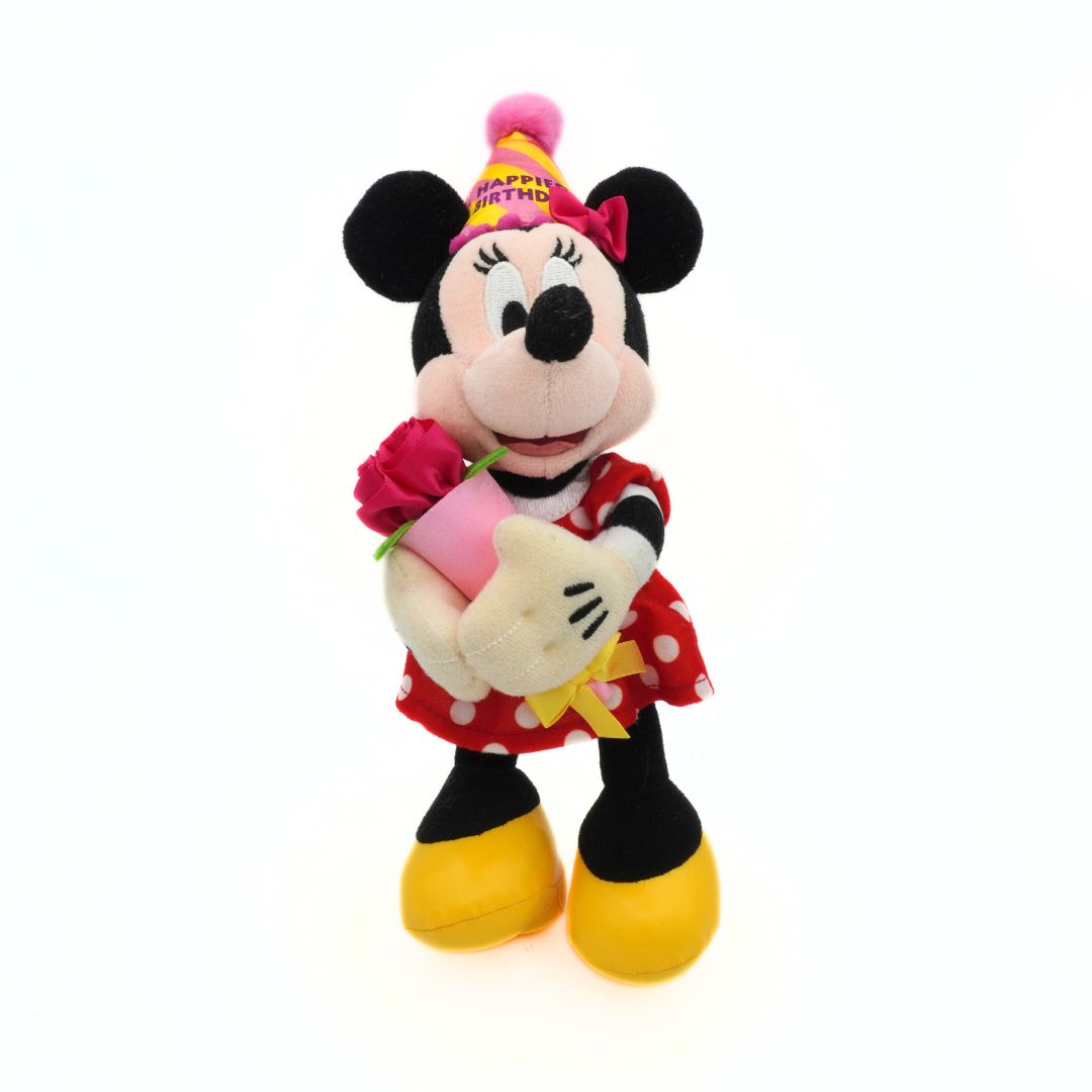 Plush toy of Minnie Mouse with a birthday hat and a red dress with a flower, on a white background