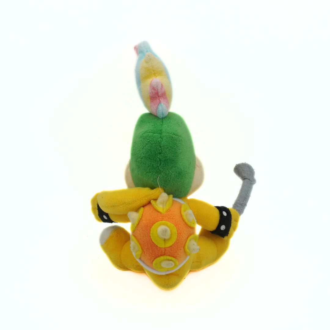 Plush toy resembling a character with green body, yellow shell, and blue head on a white background