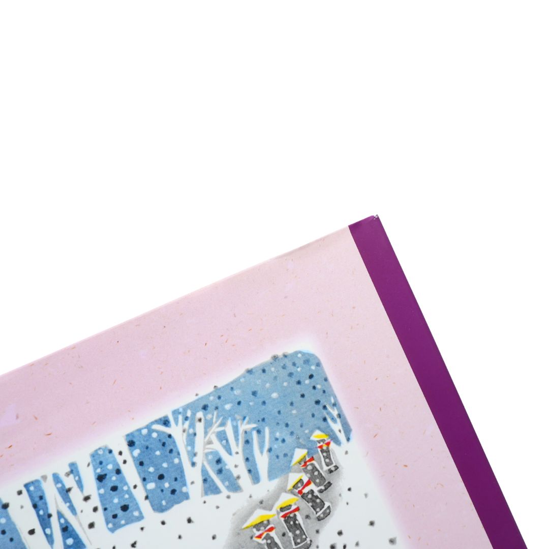 A close-up of a book featuring a winter forest scene with stylized blue trees and small colorful figures, bordered by a pink cardstock edge and a purple spine or backing on a white background.
