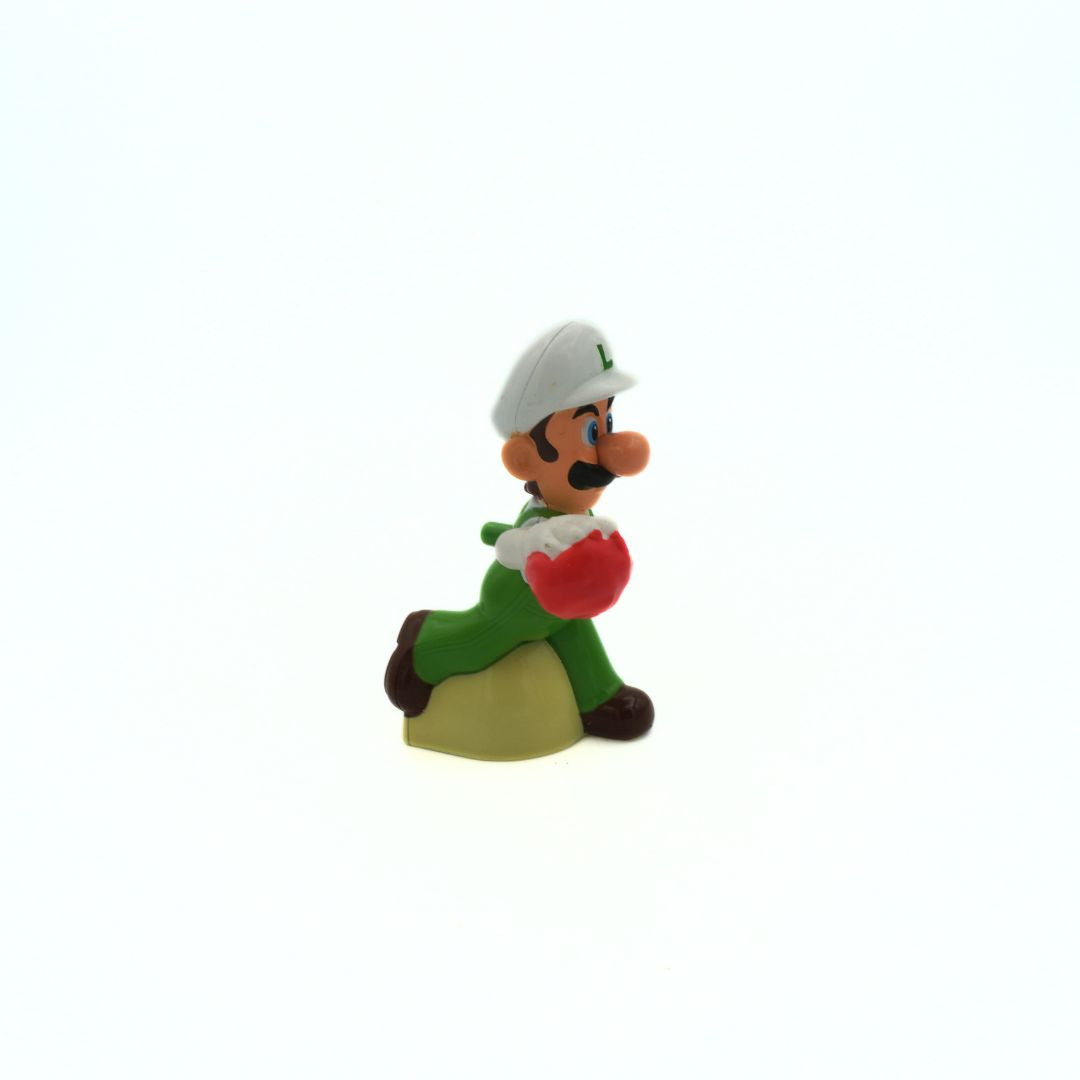 Small figurine of Luigi in green outfit with red item on white background