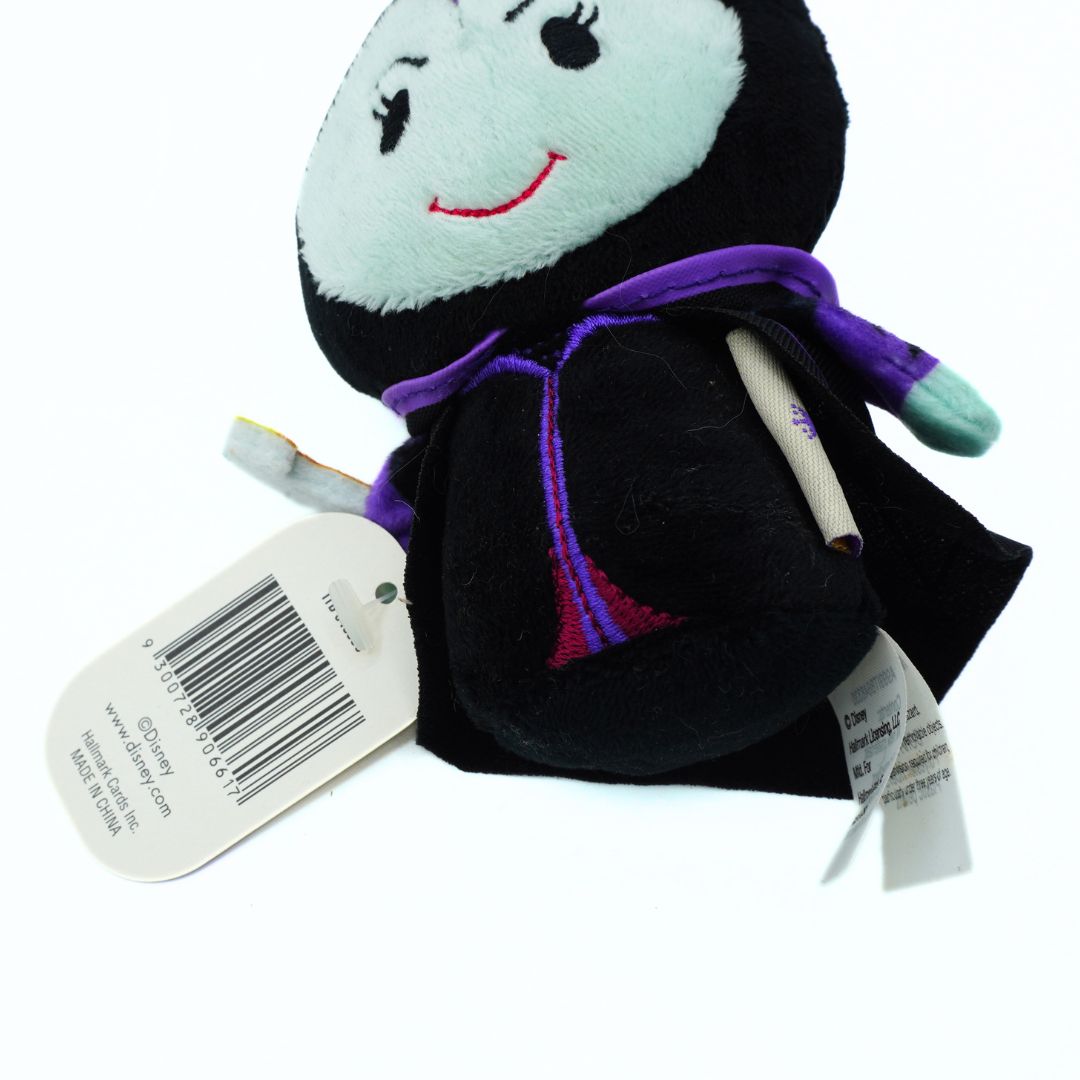 A small plush toy of a cartoon character with a black body, white face, purple scarf, and red smile, shown with a product tag on a white background.