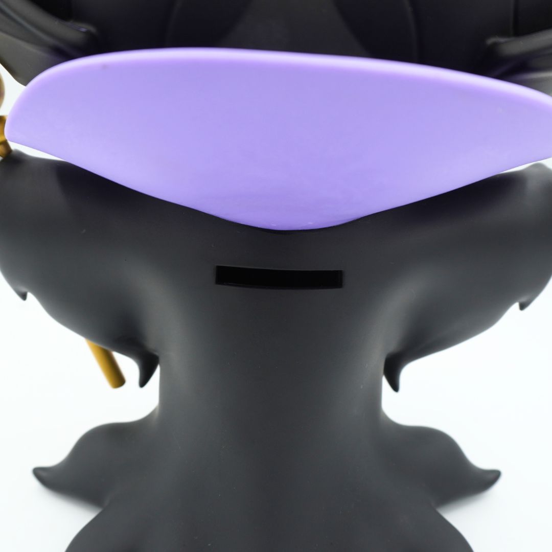 A green figurine wearing a purple and black jacket and black hat, holding a gold rod