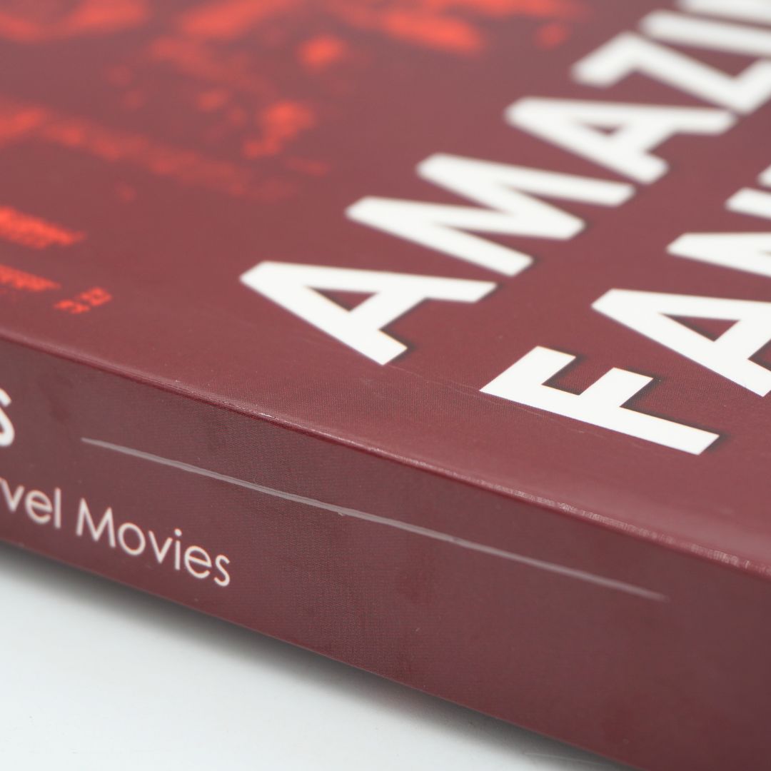 A close-up angled shot of a book cover with a deep red background, large white title text reading 'AMAZING FANTASIES,' and smaller white spine text reading 'Marvel Movies.'.