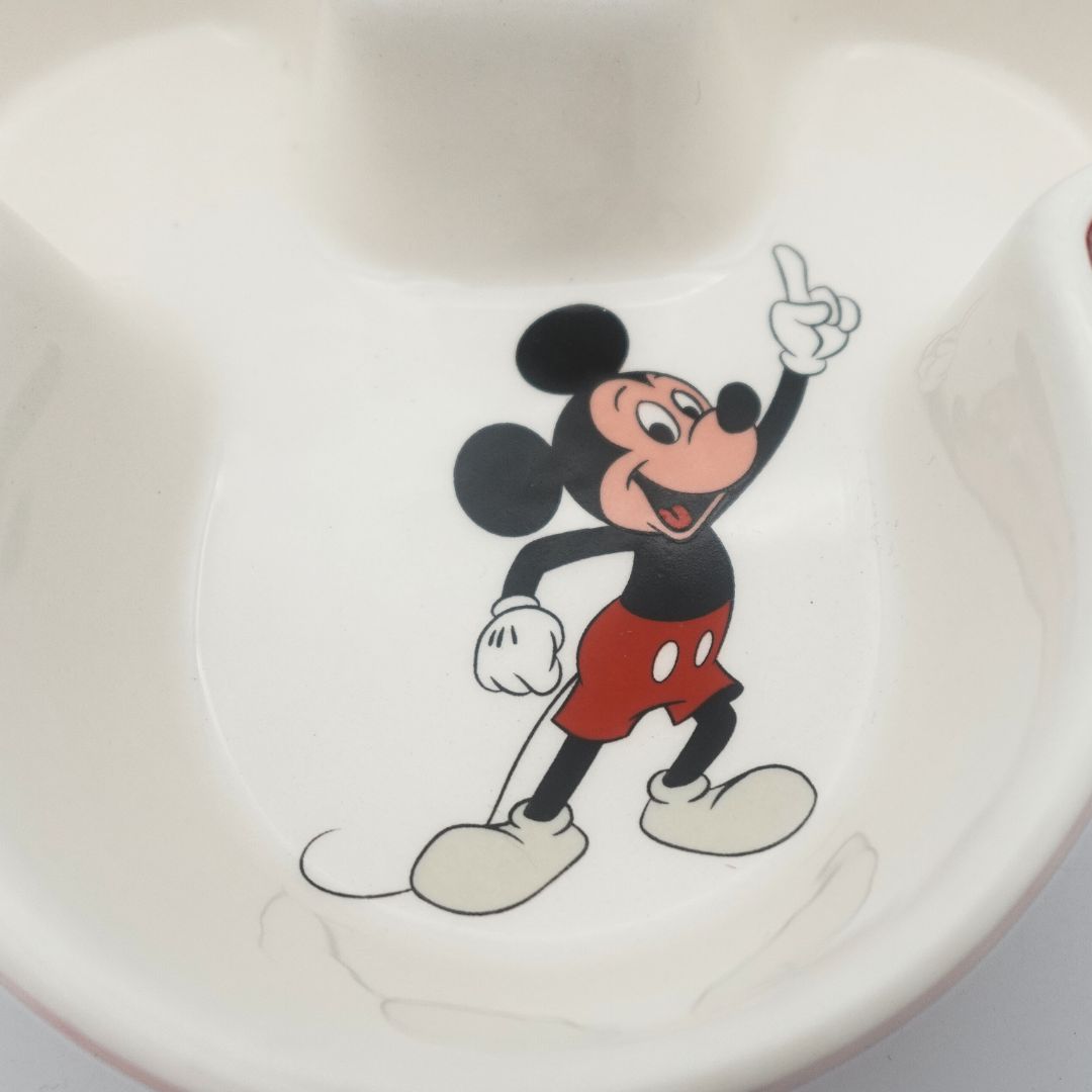 Closeup of the Mickey Mouse character at the bottom of a red and white ceramic Disney 100 bowl