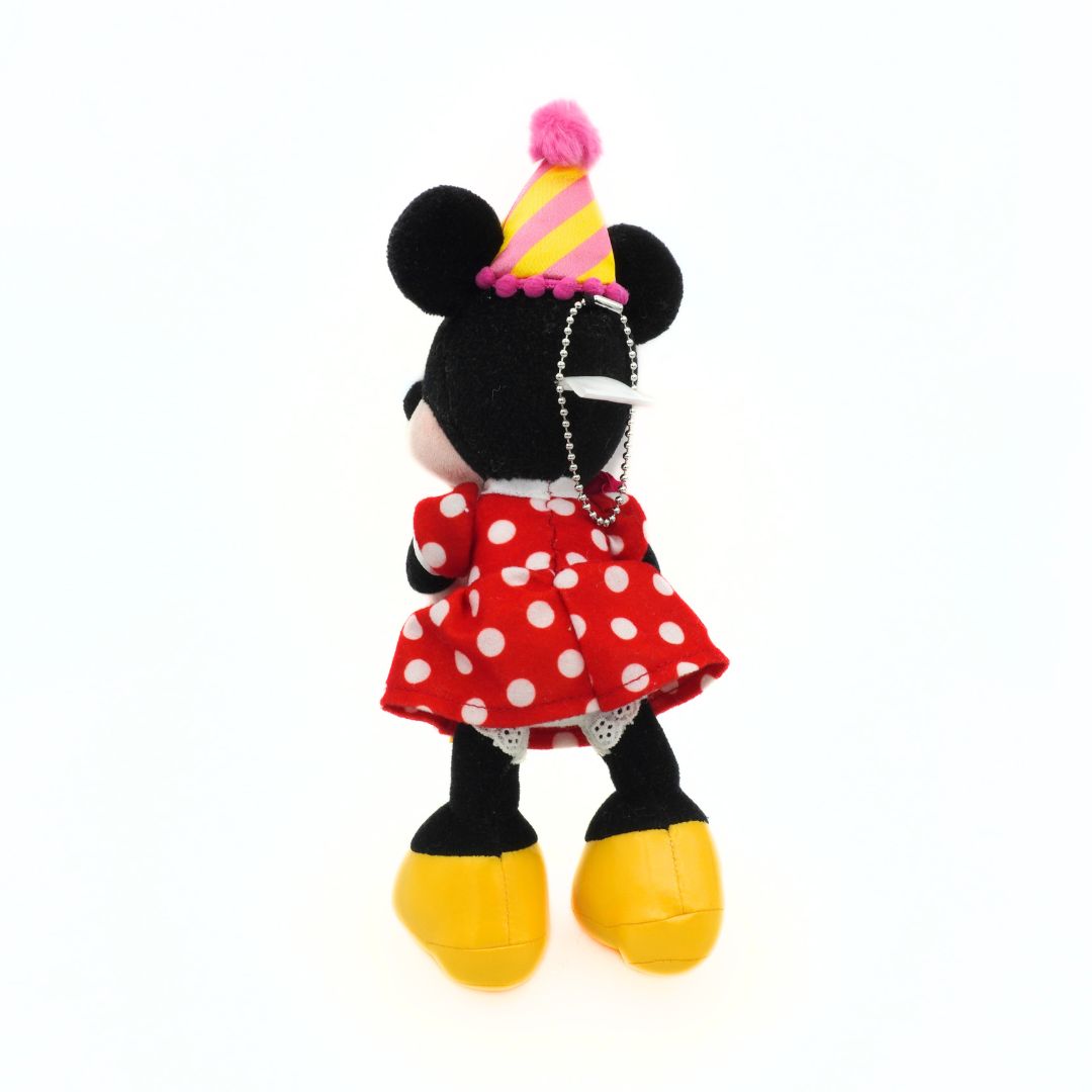 Plush Minnie Mouse toy in a red polka dot dress with a party hat on a white background