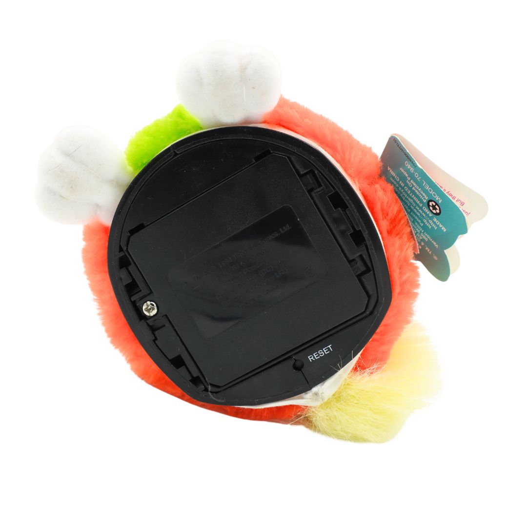 Underside of an orange and green Furby with yellow hair and blue eyes, photographed against a white background