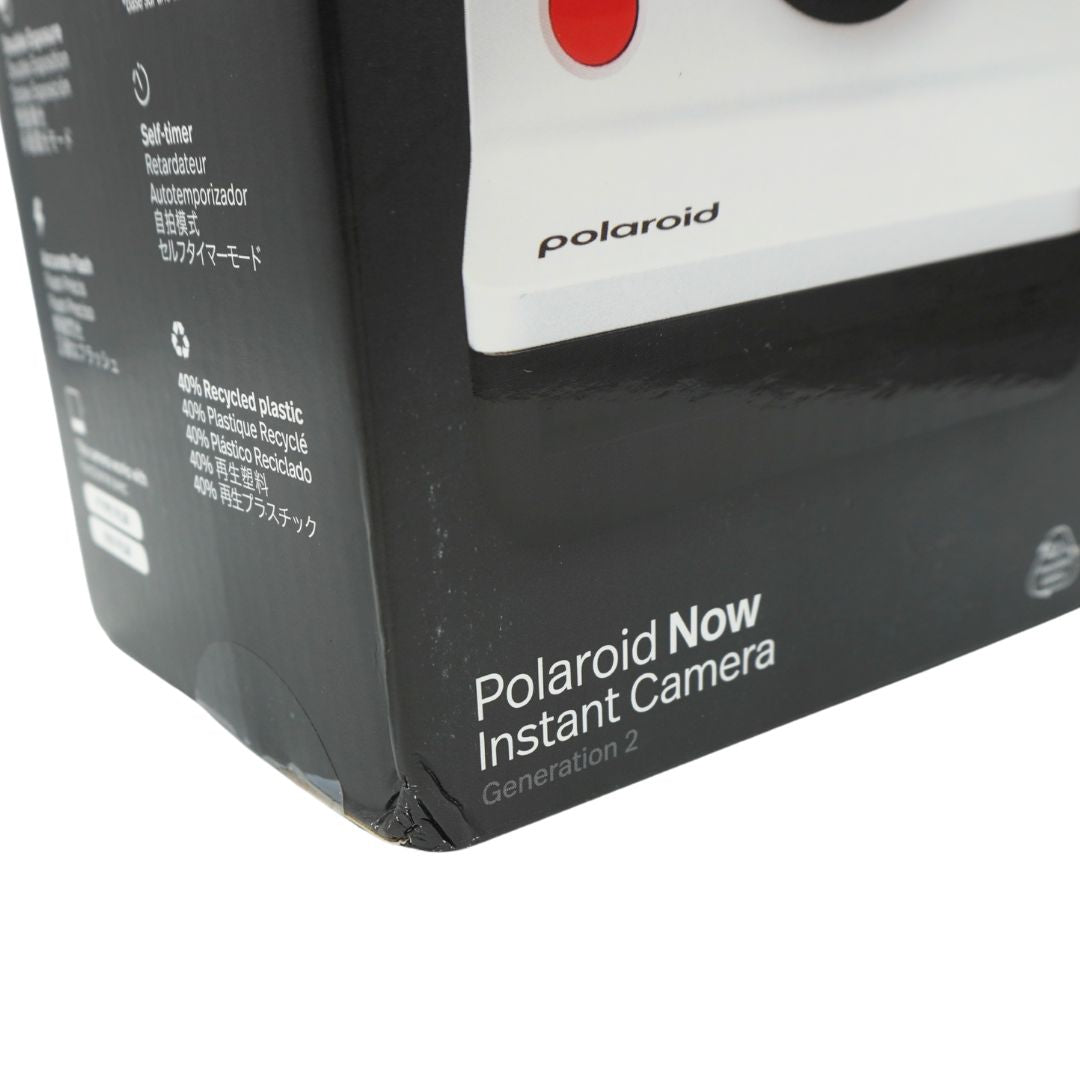 A black and white polaroid camera in a black box, titled the Polaroid Now