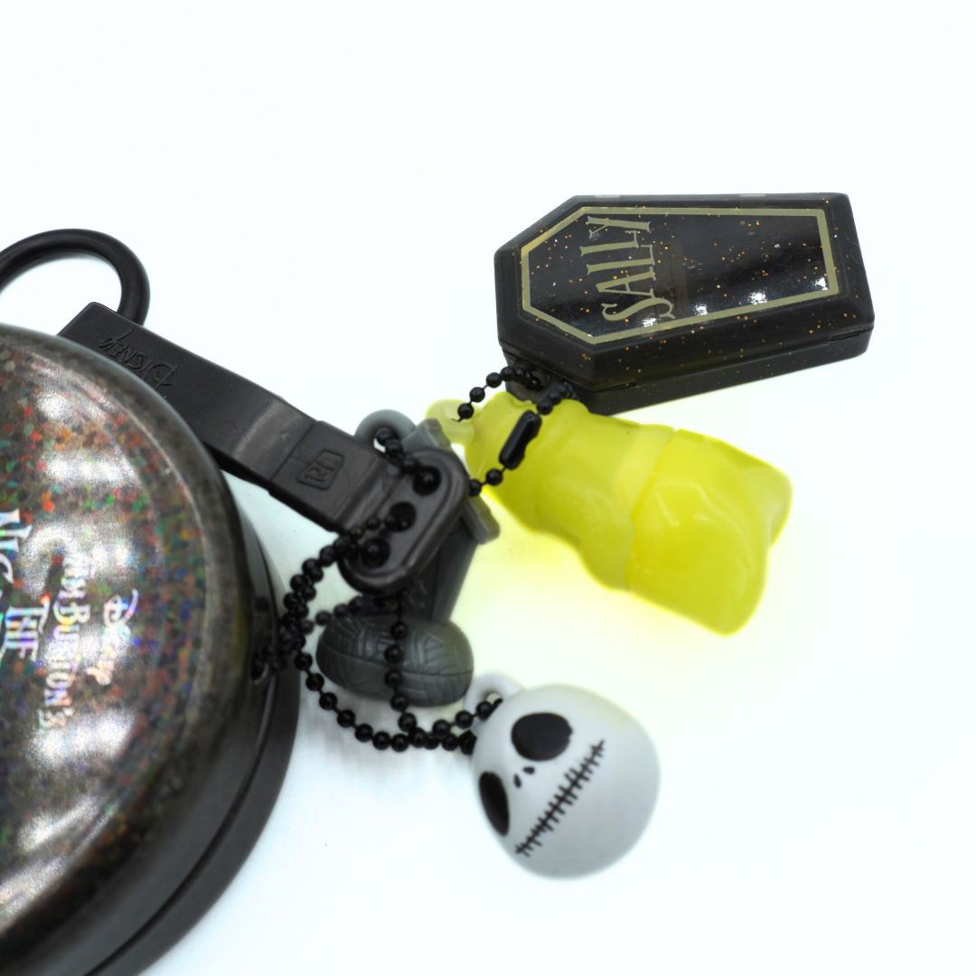 A gothic-themed keychain set featuring a black coffin-shaped tag with gold glitter and the word 'SALLY', a translucent neon yellow gummy bear, a small black skull charm, and a black beaded chain, displayed on a clean white background.