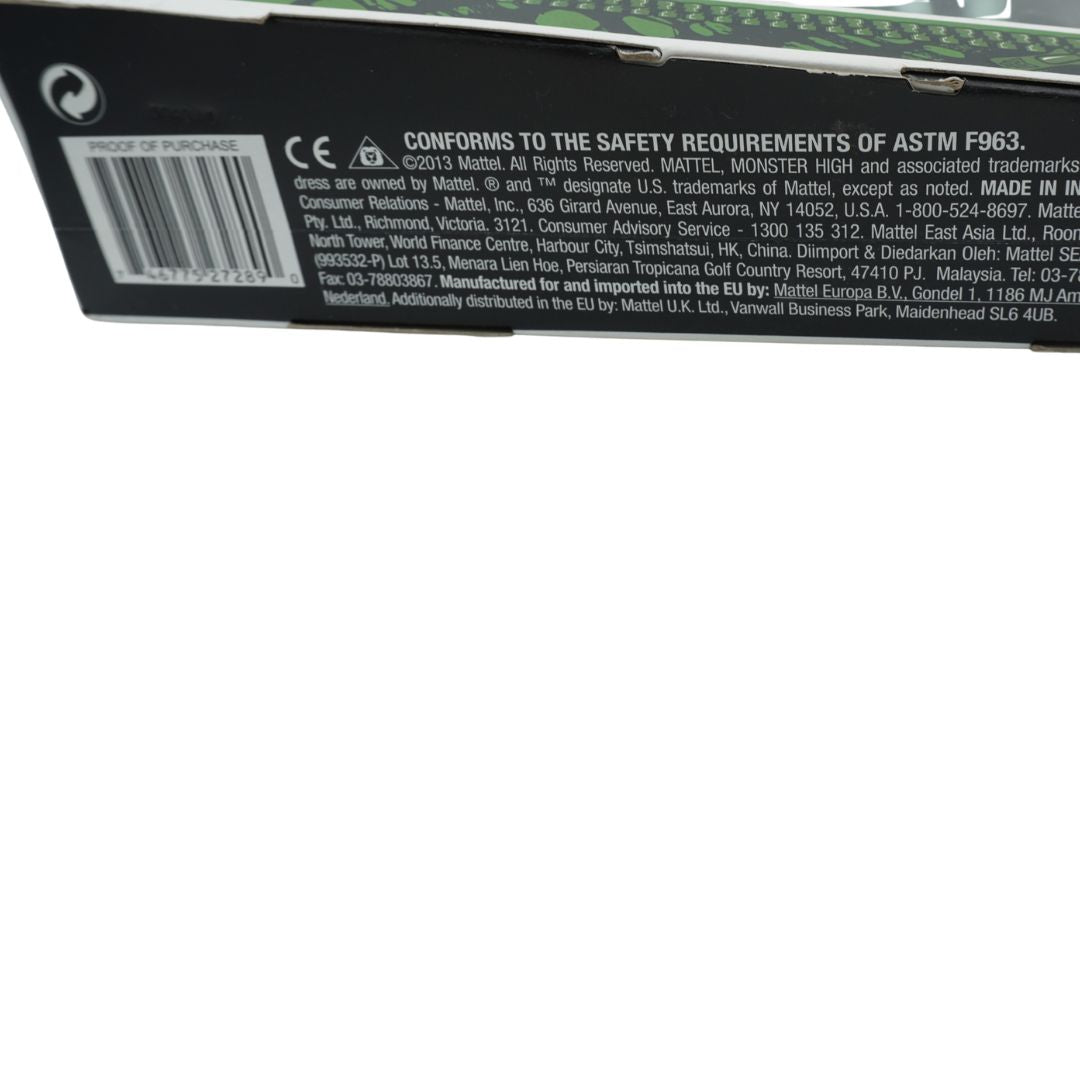 Close-up of the bottom edge of a black Mattel product box showing printed safety information, a barcode, and small green circuit-board-like graphics along the top edge, against a white background.