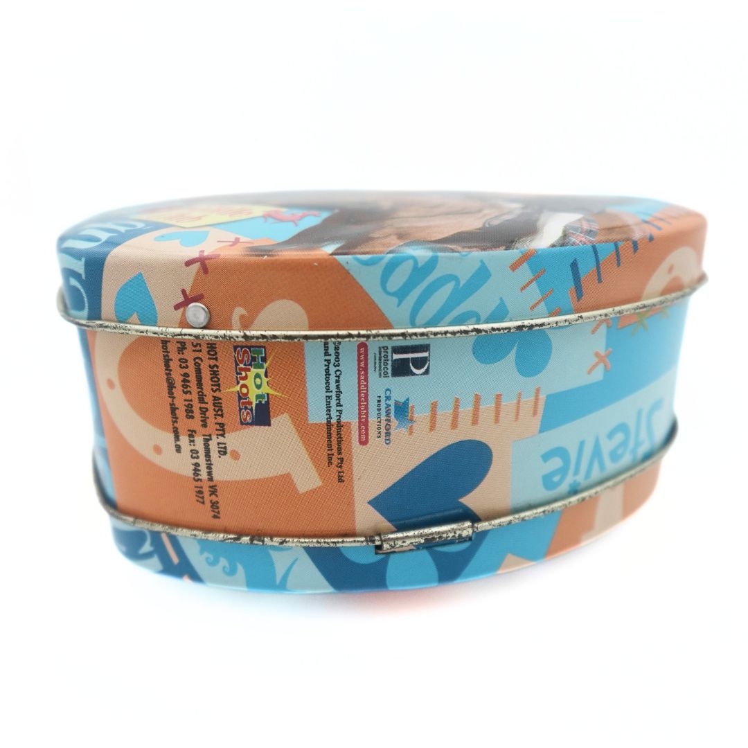 Hot Shots branding and copyright information seen on the side of the 2003 Saddle Club tin bag featuring a blue and orange colour palette