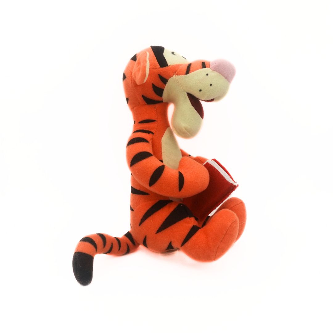 Side on photo of a Winnie the Pooh's Tigger plush holding a red book