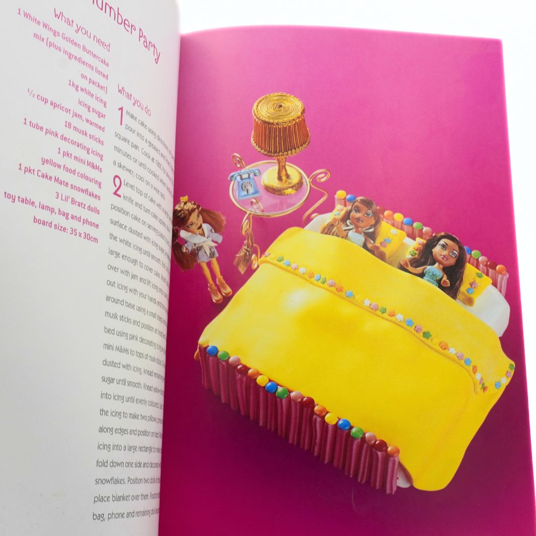 Open Total Girl cookbook with a colourful illustration of a yellow cake and Bratz dolls on a pink background