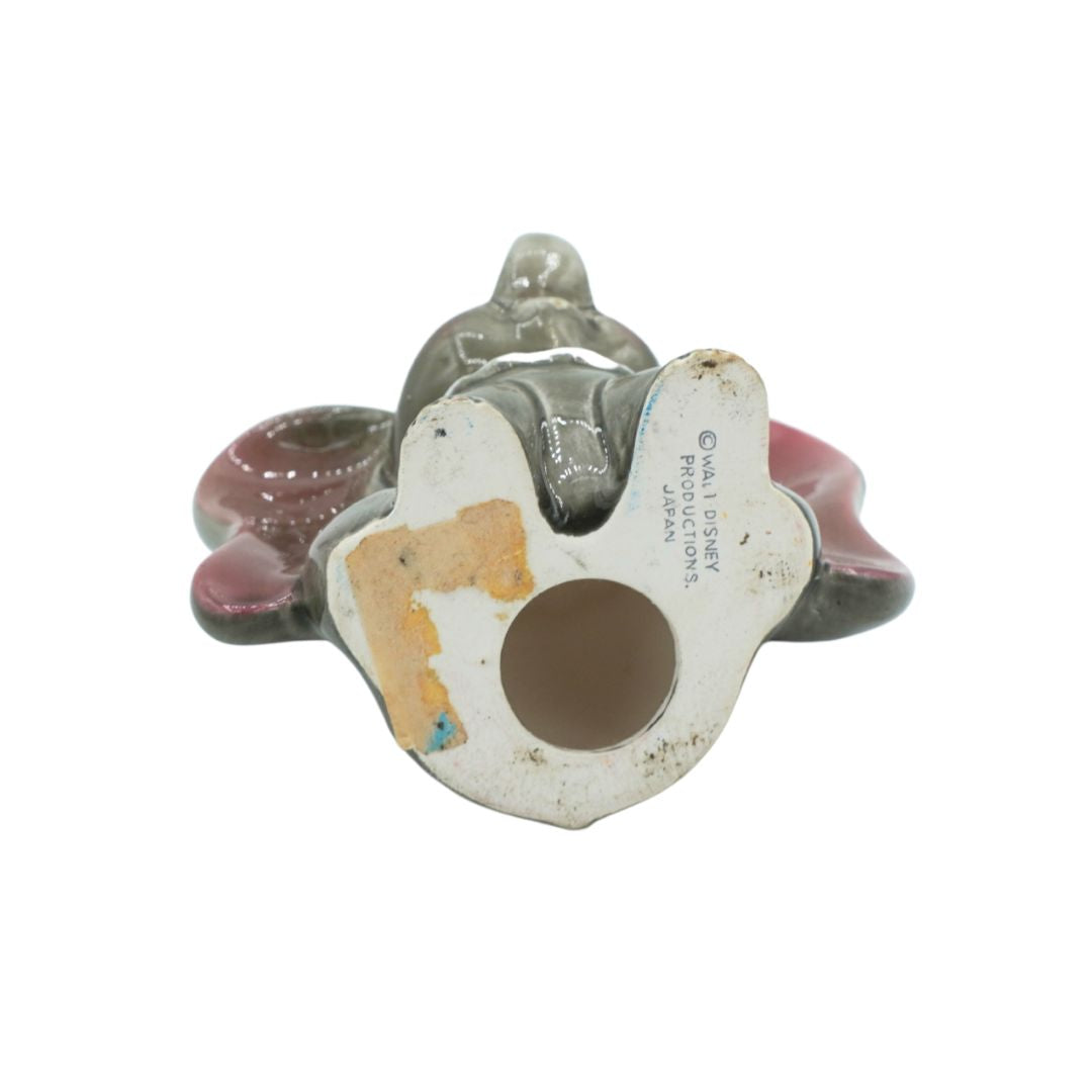 A vintage Japanese ceramic figurine of a seated figure on a cloud, shown from the underside. The figure is gray glazed, seated on a pink cloud, with a white base featuring printed Japanese text and a circular hole.