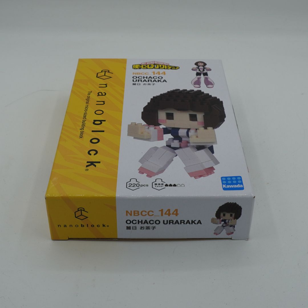 A boxed nanoblocks figurine of Ochaco Urakawa, model NBCC 144. The packaging is white and yellow, featuring a 3D-rendered image of the assembled blocky character.