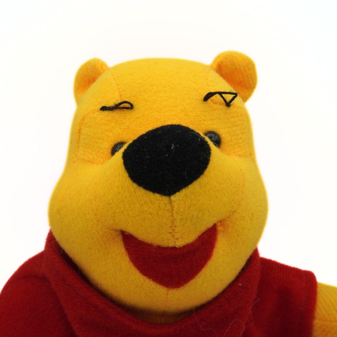 Close-up of a Winnie the Pooh plush toy with a red scarf on a white background