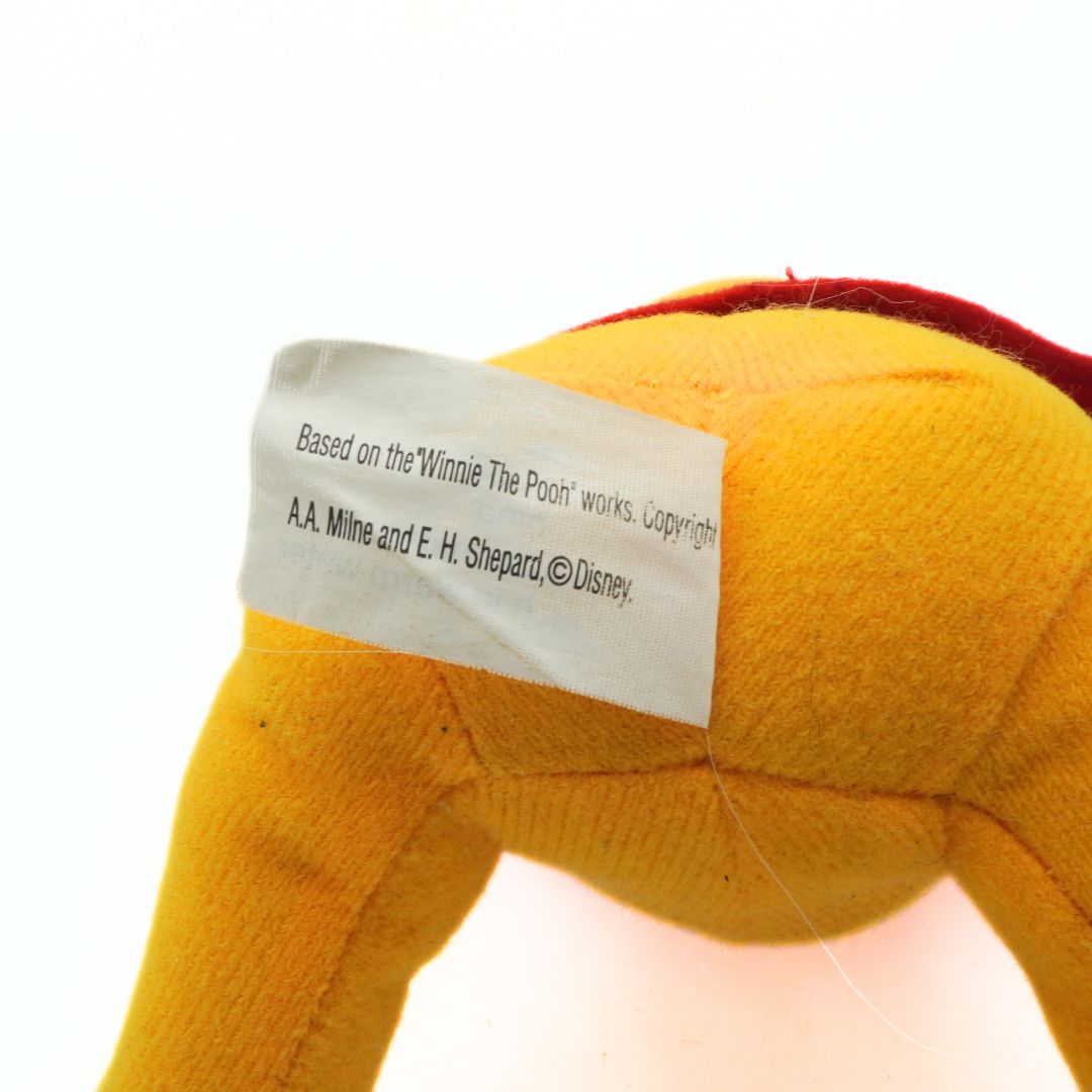 Close-up of a Winnie the Pooh plush toy with a label on a white background