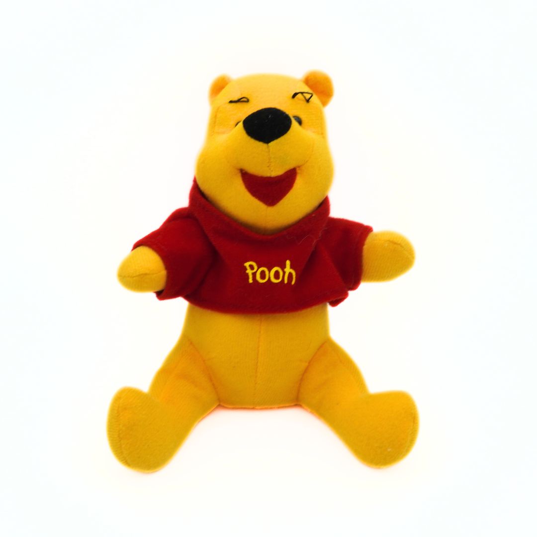 Plush toy of a bear character wearing a red shirt with 'Pooh' on it against a white background