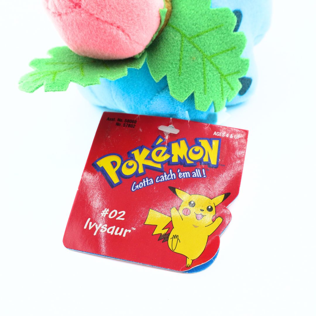 Plush toy of Ivysaur from Pokémon with red packaging featuring Pikachu on a white background