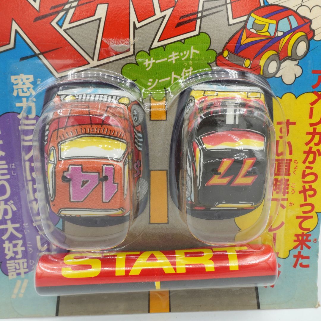 Two toy cars in packaging with a colorful background featuring Japanese text and graphics.