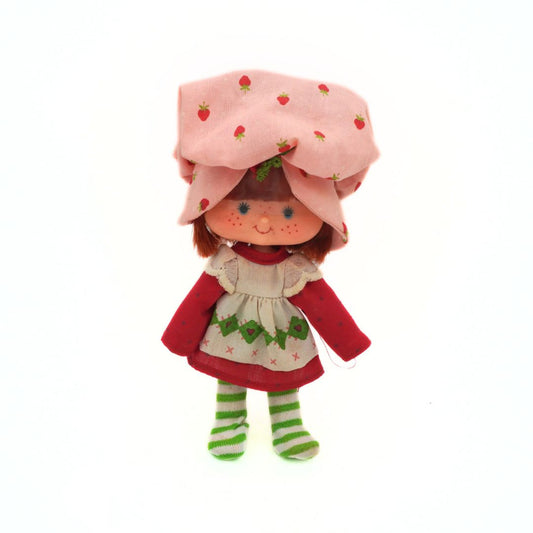 Plush toy resembling a character with a strawberry-themed hat on a white background