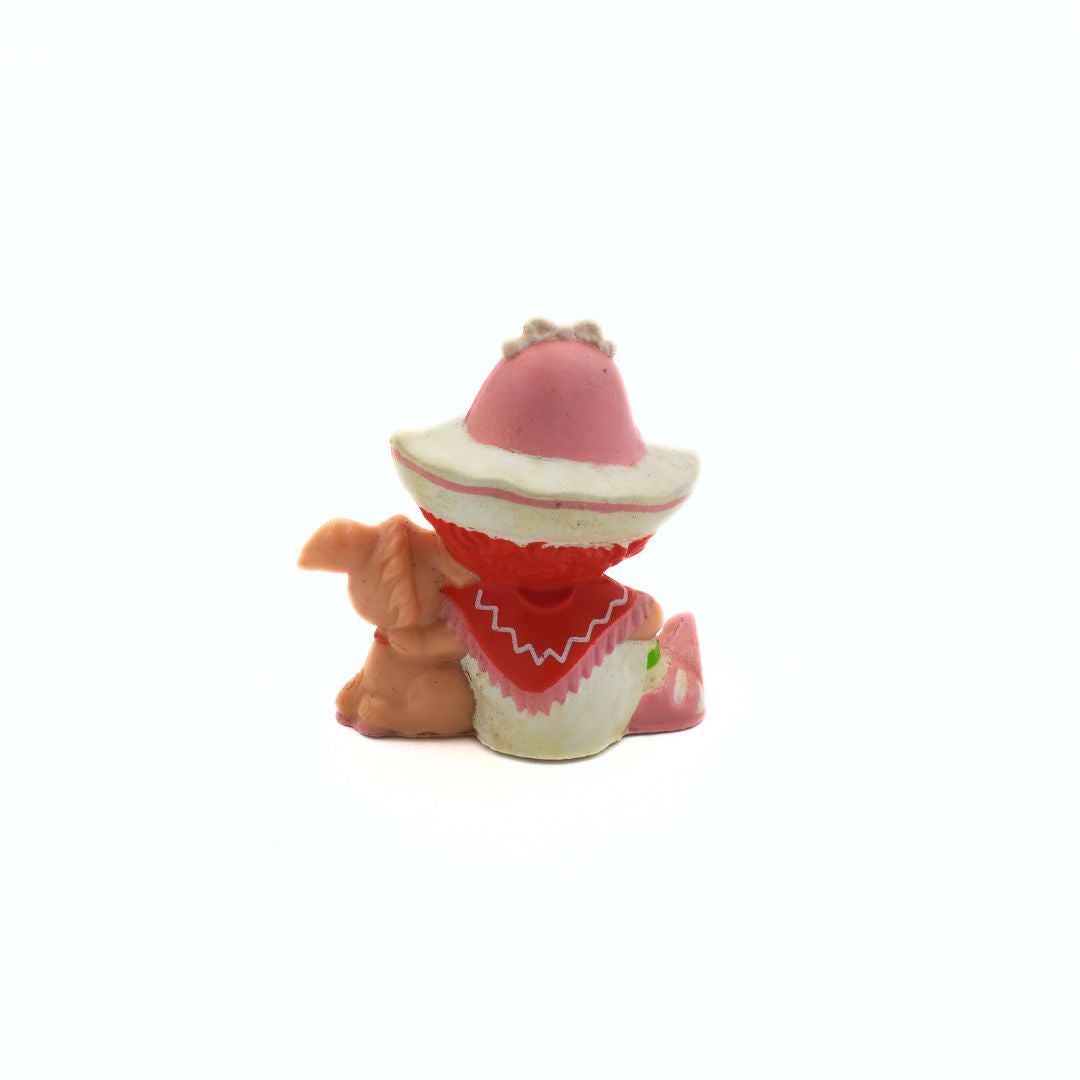 Small figurine of a character wearing a pink hat and red outfit on a white background