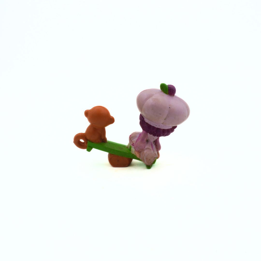 Two small plastic figurines, one brown and one pink with a purple scarf, on a white background.