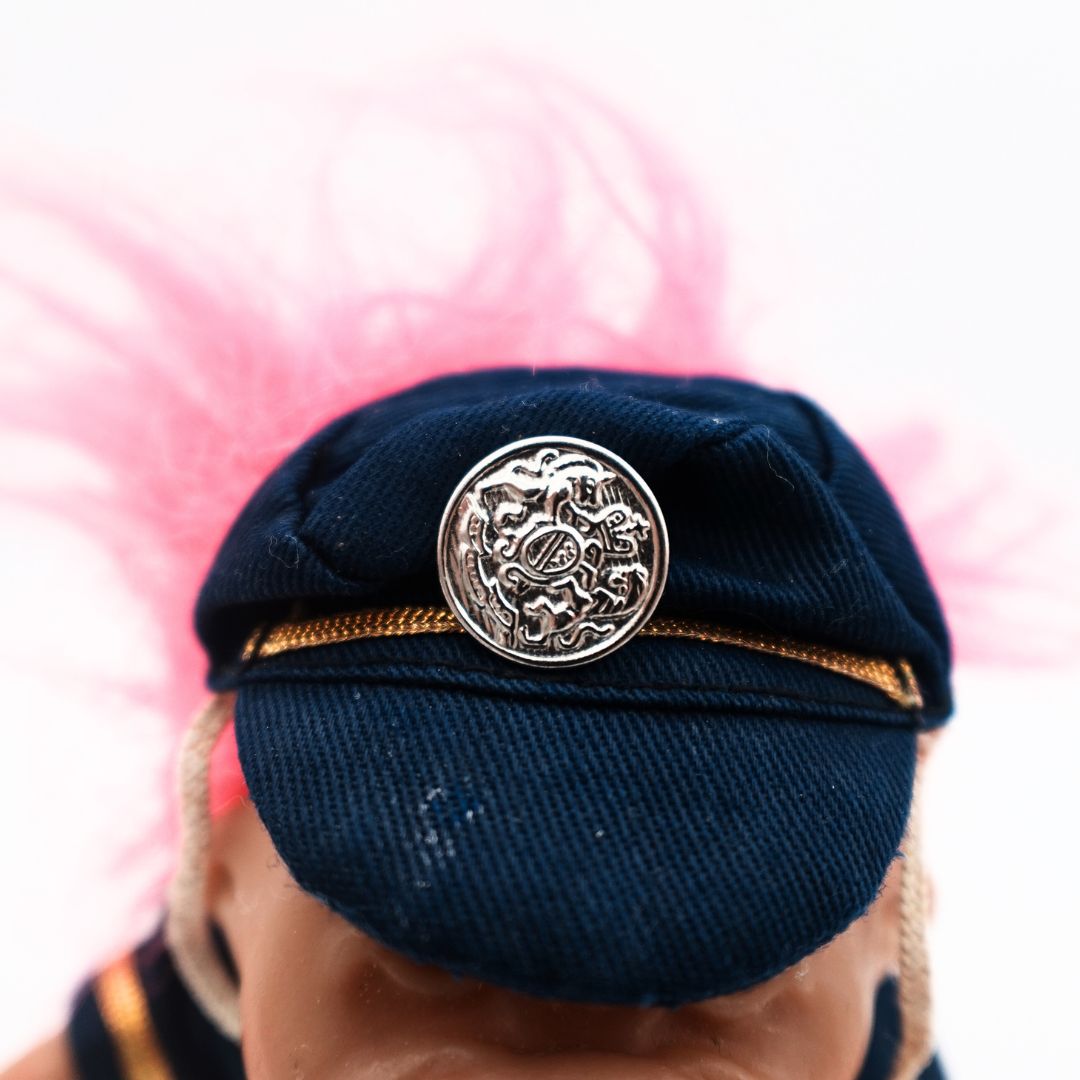 Closeup of the 1986 Policeman Troll Dolls hat, blue in colour with gold trim and a silver badge