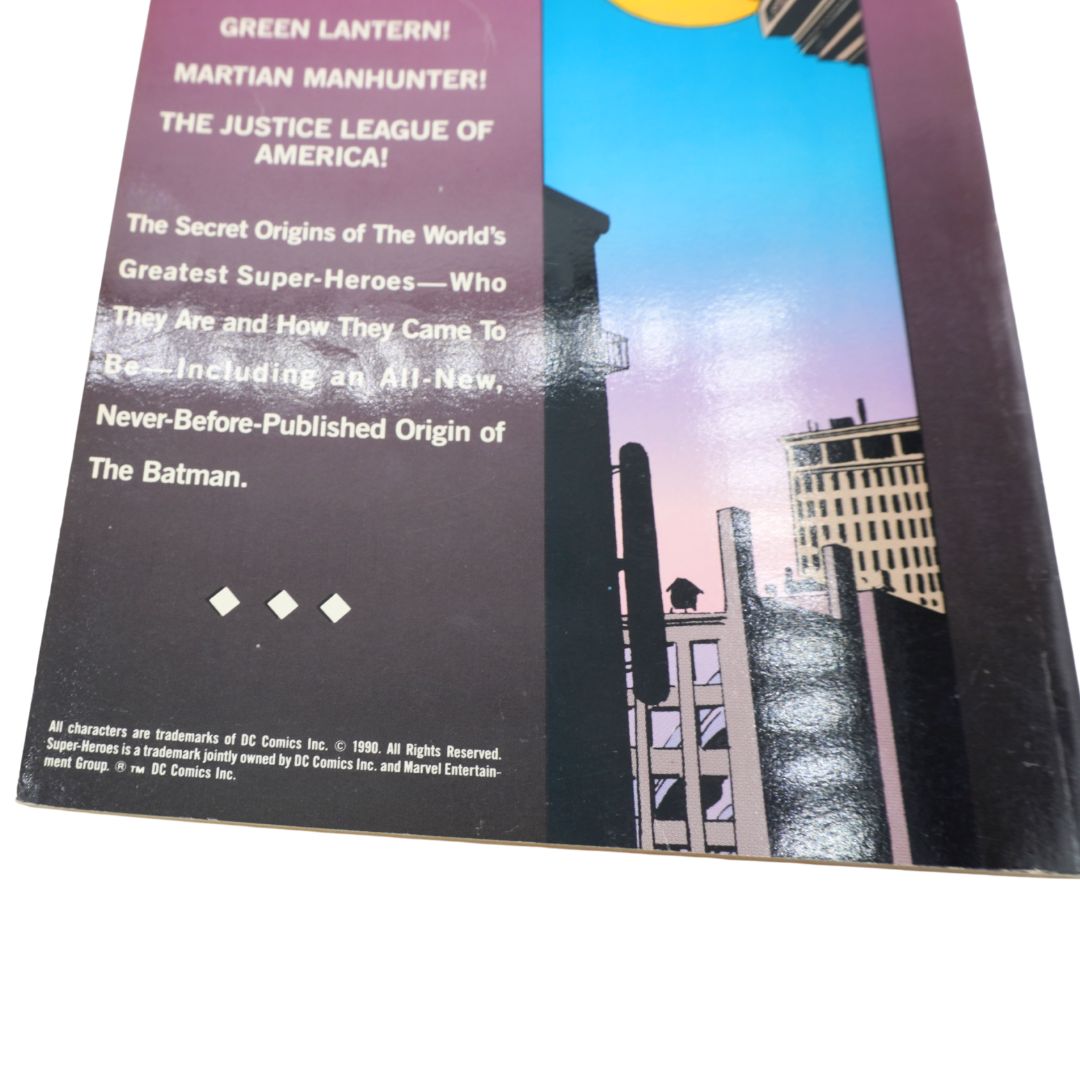 A close-up of a comic book cover or booklet page with printed text on a dark panel and an illustrated cityscape in blue, purple, and beige tones. Visible text references Batman and DC Comics.