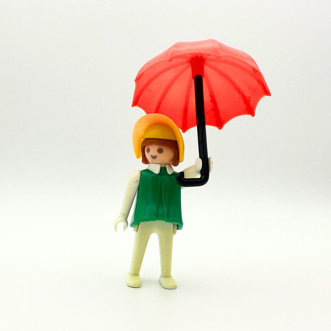 70's Geobra doll with a red umbrella, yellow hat, green shirt and white pants. She has brown hair