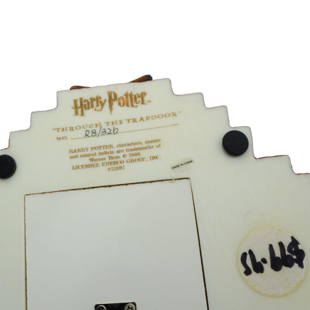 A close-up of a Harry Potter themed product, likely a collectible plaque or display piece, featuring the 'Through the Trapdoor' text and Warner Bros. / Harry Potter licensing text on a cream-colored background.