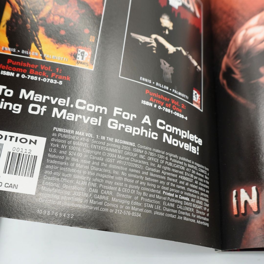 A close-up of a printed book or comic issue spread, showing the back cover with barcode, publisher text, and partial front cover art with a dark red and black design.