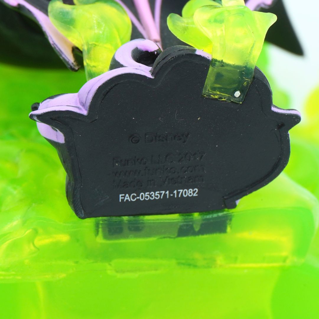Close-up of a Disney Funko collectible figure accessory, showing the black molded base with embossed Disney and Funko branding, attached to translucent neon green and purple plastic flower-like elements.