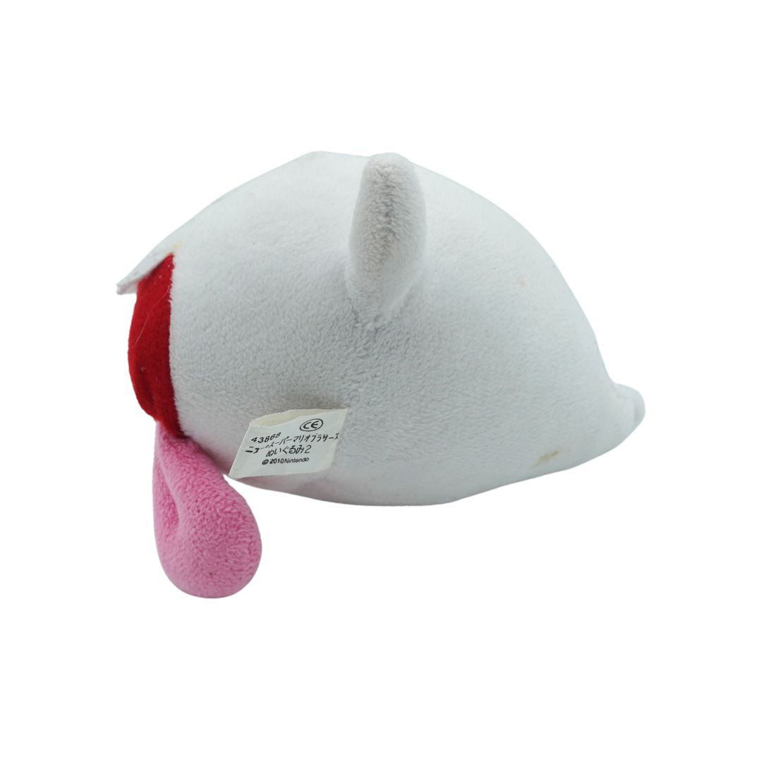A white plush toy shaped like a stylized character head, shown from the side on a plain white background. It has a red inner side, a pink protruding tongue, and a small sewn-in label.