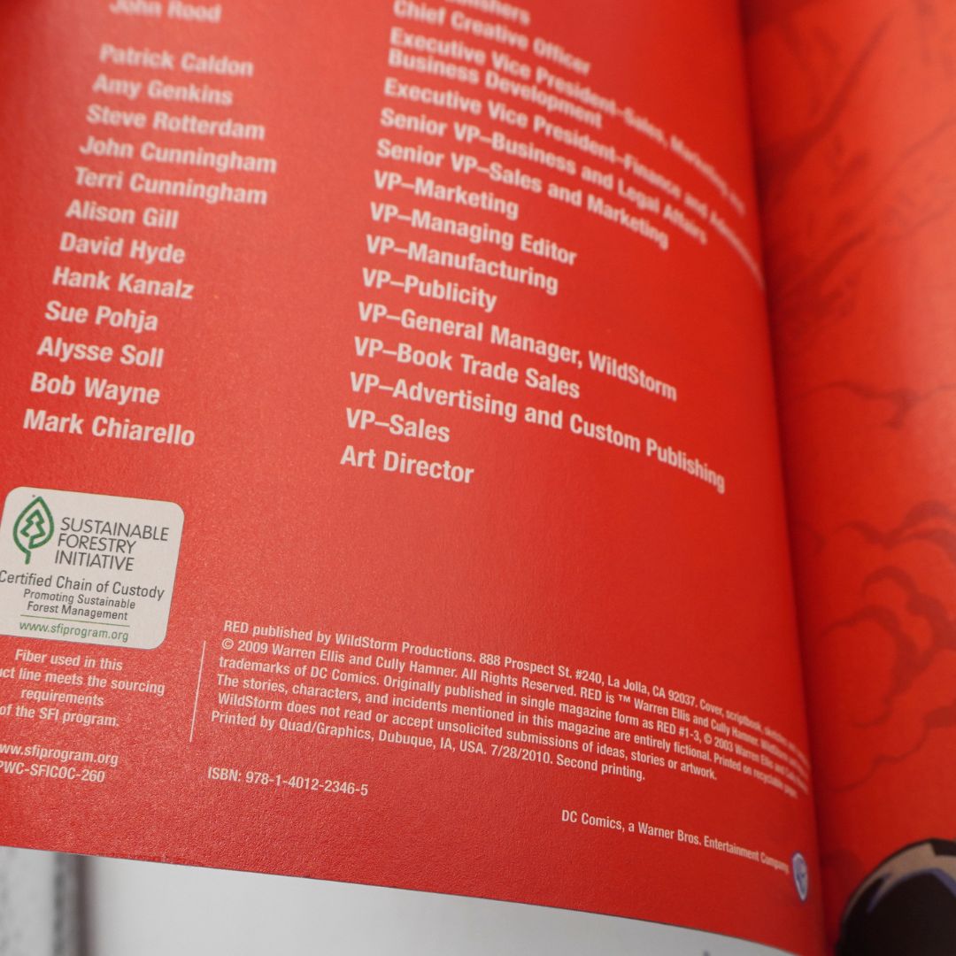 Close-up of a red printed book or magazine page with a list of company names and a Sustainable Forestry Initiative seal, photographed at an angle.