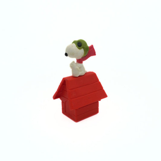 Snoopy figurine on a red doghouse with a green hat and red scarf on a white background