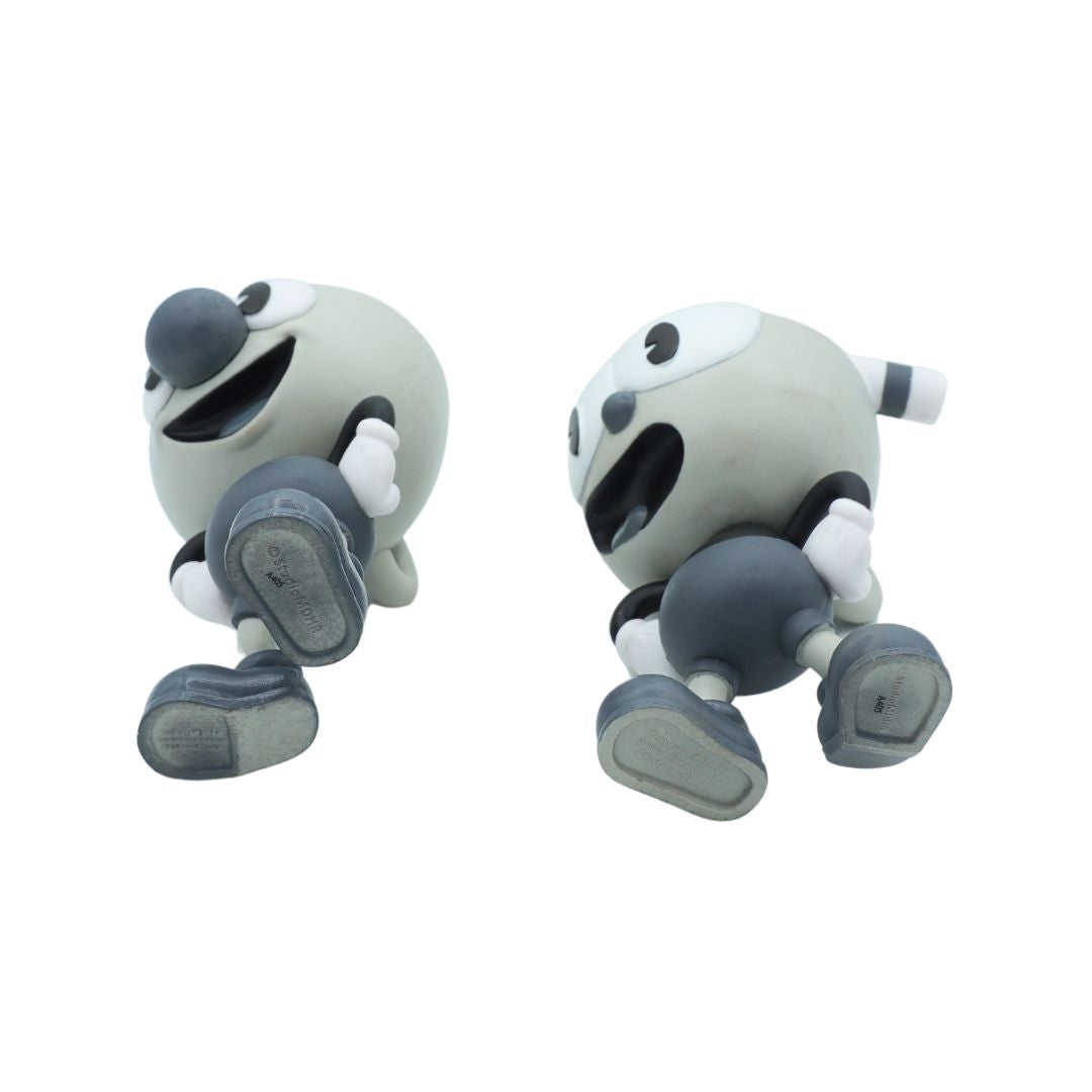 Two small cartoon character figurines shown side by side on a plain white background. The characters have round pale gray heads, dark gray/black facial features and limbs, and white gloves, with one figure facing left and the other facing right.
