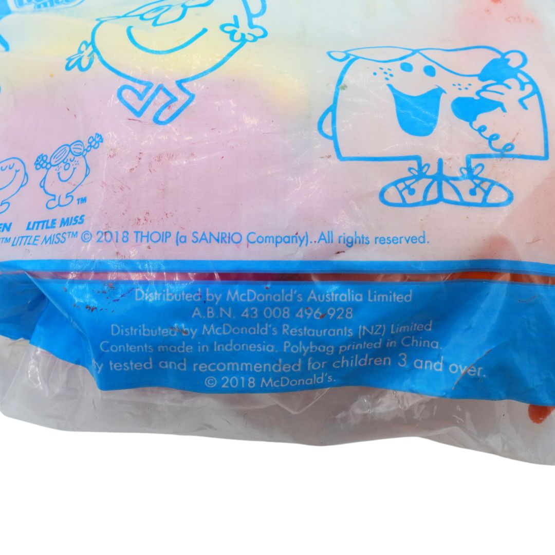 A close-up of a packaged toy or collectible item in a clear plastic bag with blue printed cartoon graphics and text. Visible text includes 'LITTLE MISS' and '© 2018'