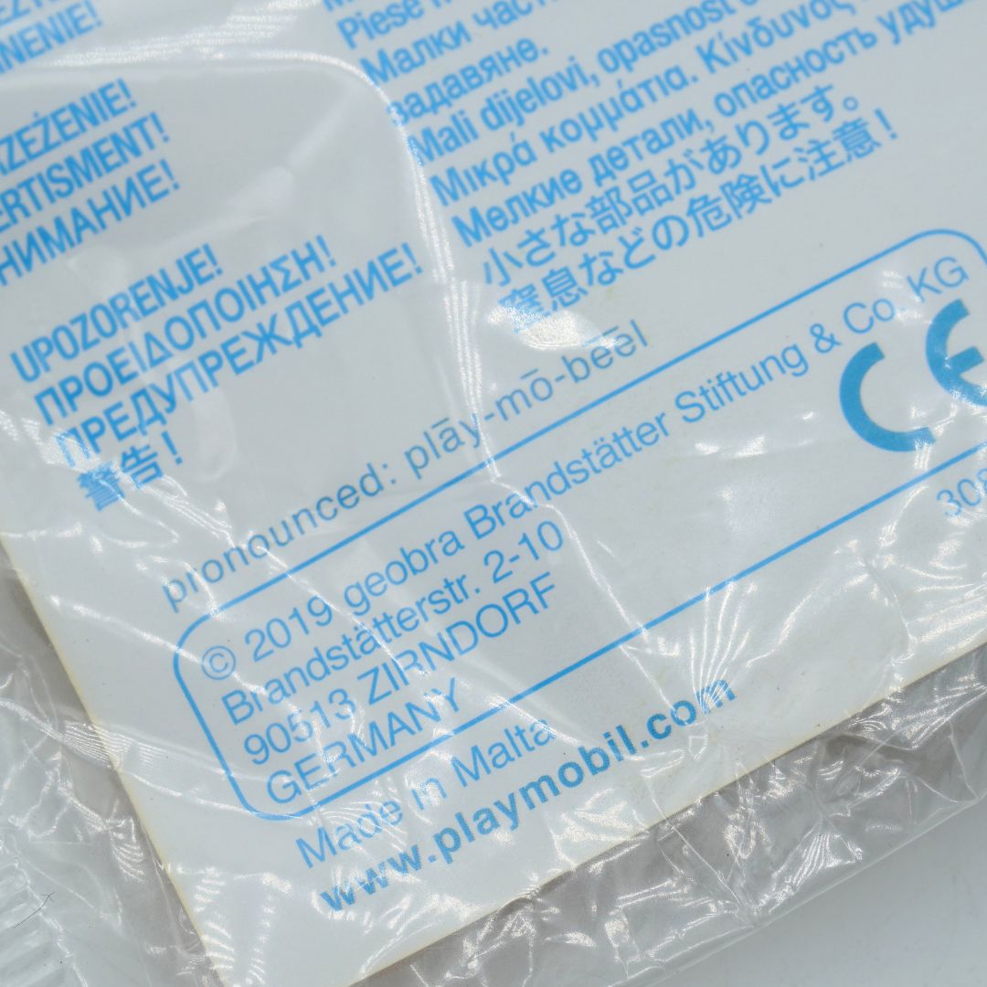 Close-up of a white plastic-wrapped product package with blue printed text and a CE mark, showing the brand name playmobil and website www.playmobil.