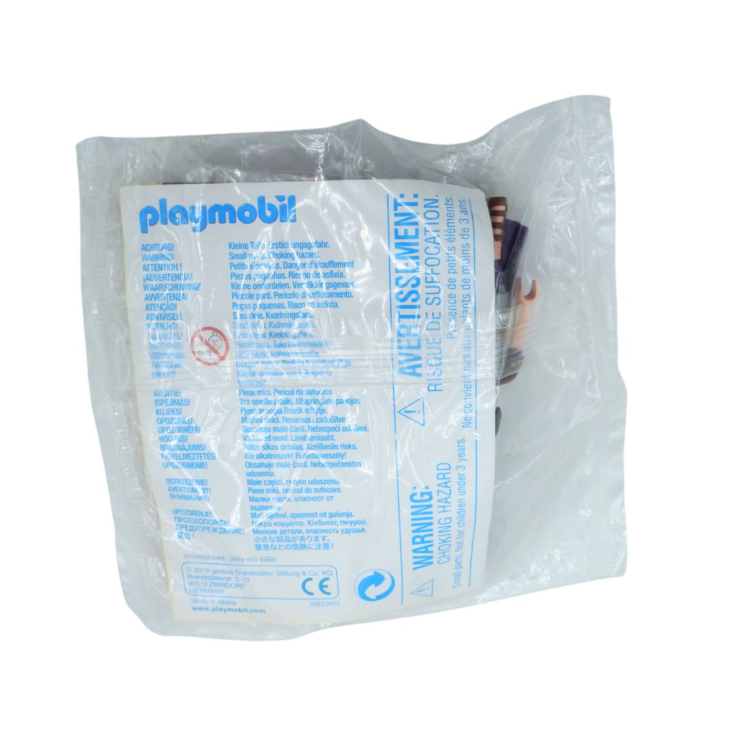 A packaged Playmobil toy figure sealed in a clear plastic bag with a white printed instruction and warning label. The blue Playmobil logo is visible on the label, and part of the figure is visible through the transparent packaging.