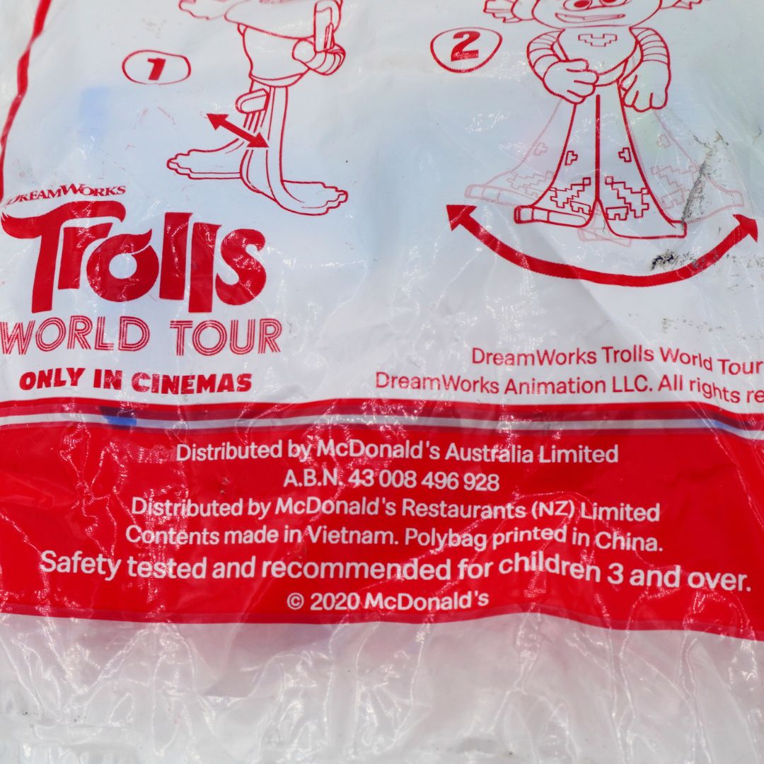 A close-up of a plastic bag printed with DreamWorks Trolls World Tour packaging text and red line drawings on a mostly white and red bag.